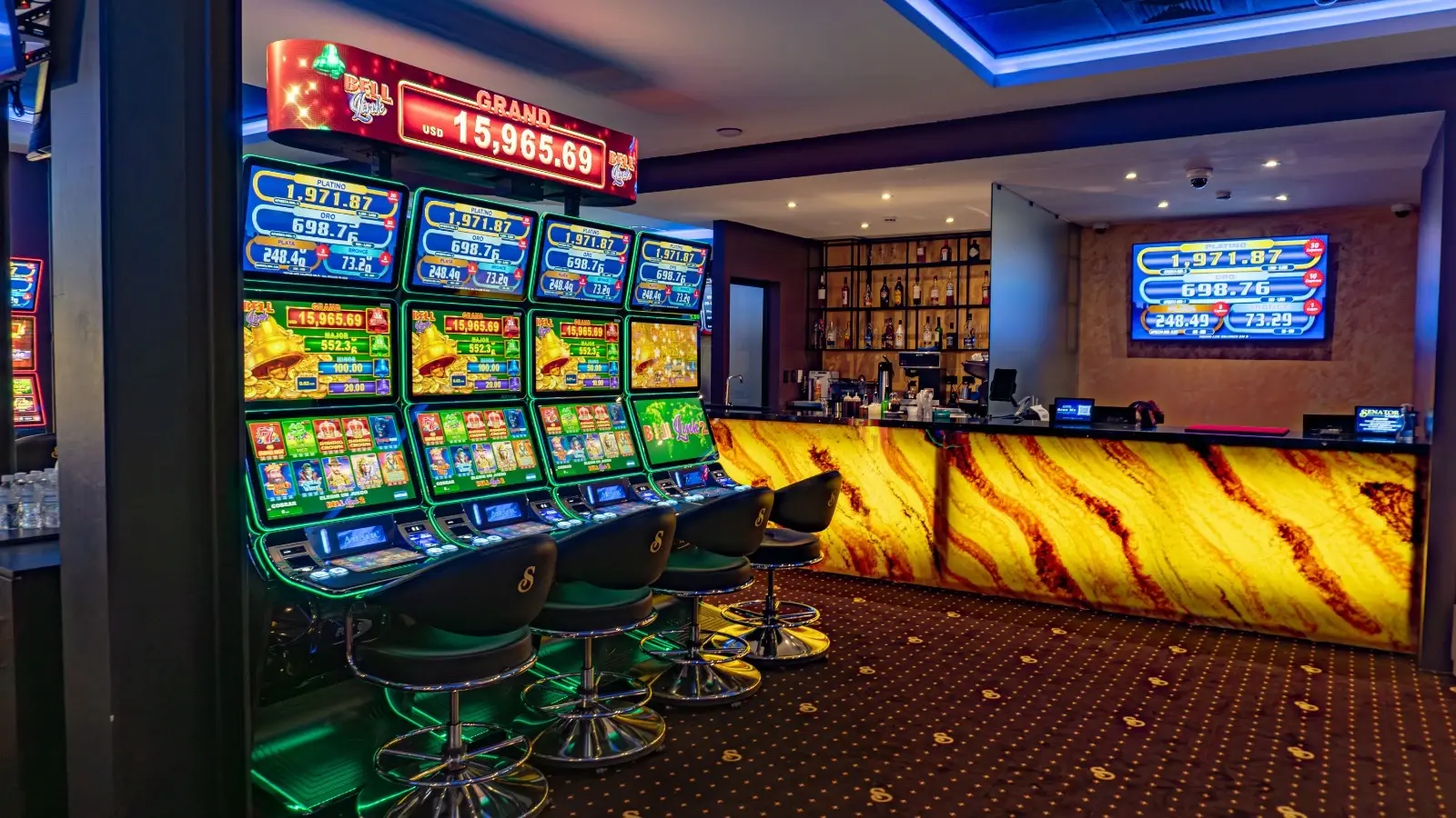 The bar at Casino Senator La Joya, its counter front lit amber, with a bank of slot machines and stools along the wall to the left