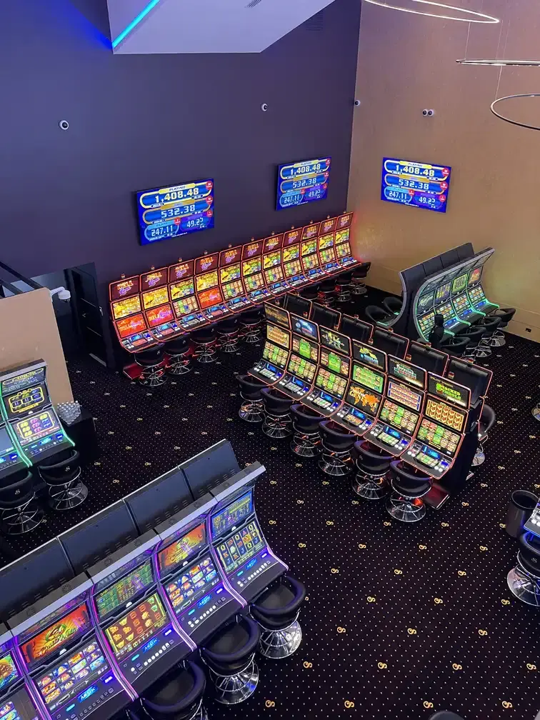 The gaming floor at Casino Senator La Joya seen from above, curved rows of slot machines on patterned carpet below three jackpot screens