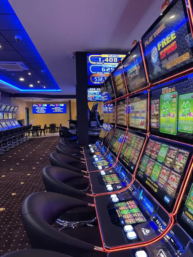 A long row of slot machines and leather stools at Casino Senator La Joya, lit by a blue ceiling cove