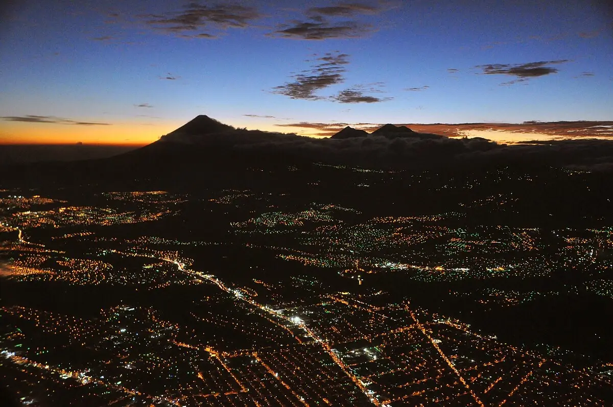 A Guatemalan city at dusk, with volcano peaks on the horizon