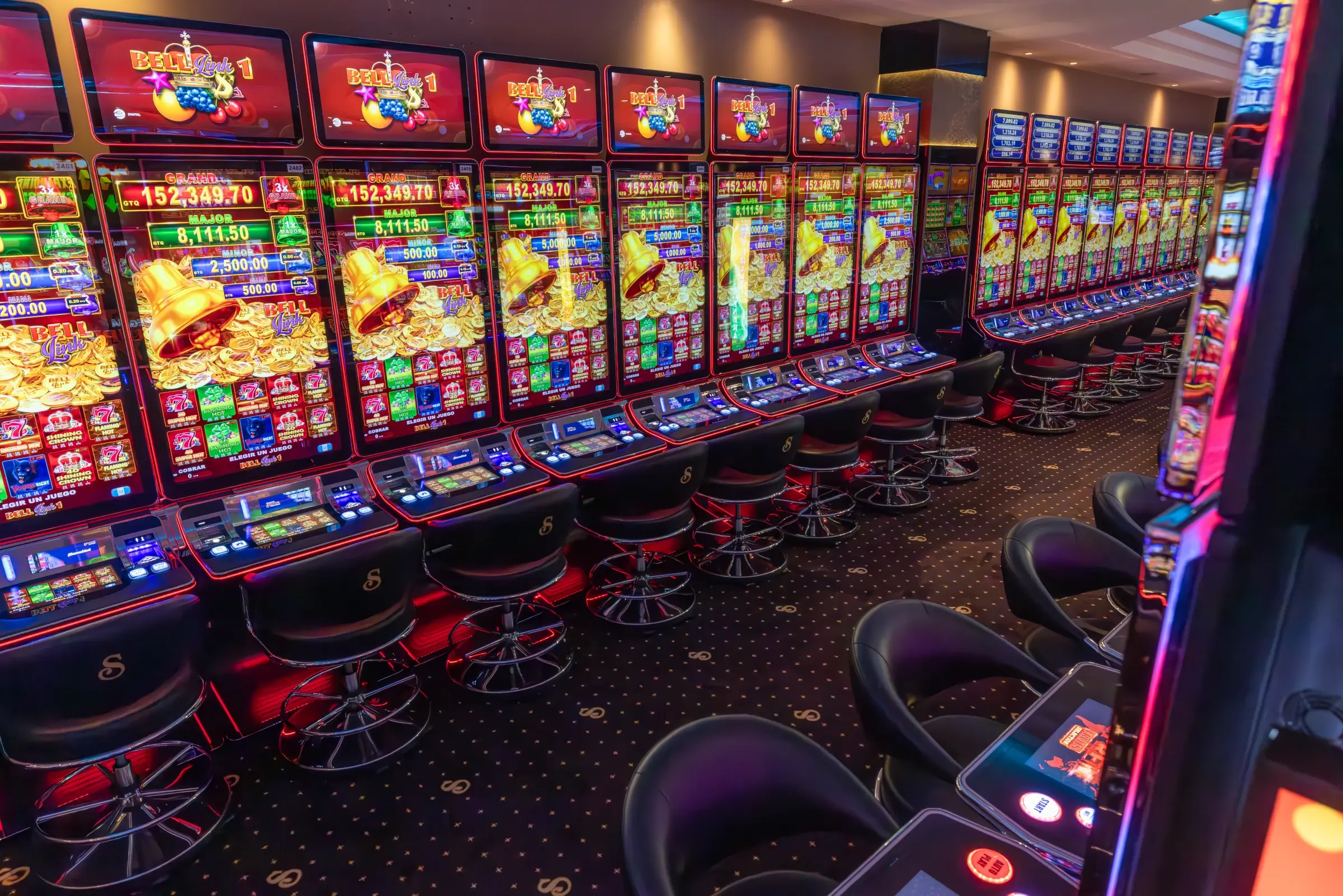 A long row of machines with linked jackpot totals climbing on the screens above the reels, Guatemala