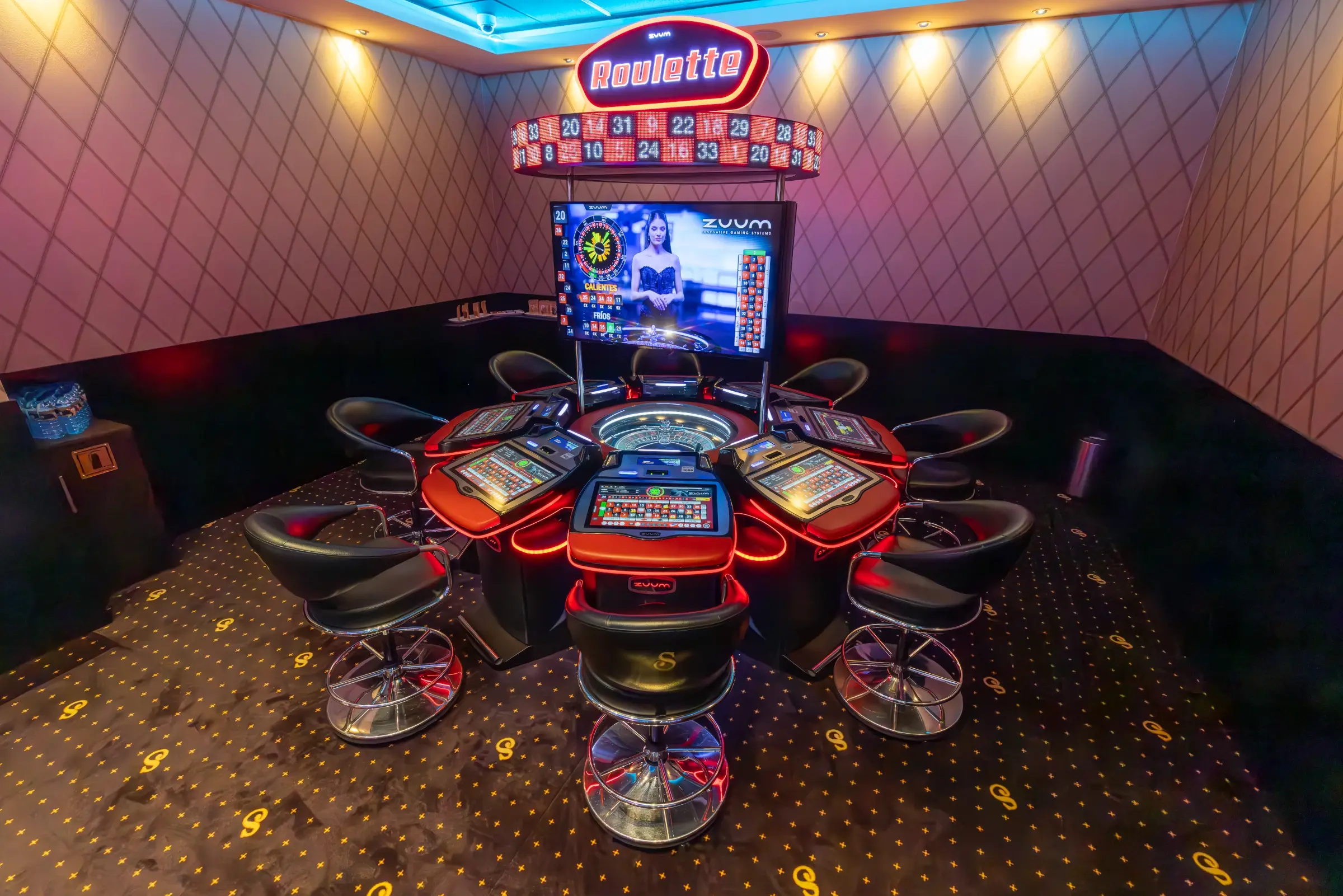 An electronic roulette wheel ringed by player stations under a lit Roulette sign, Guatemala