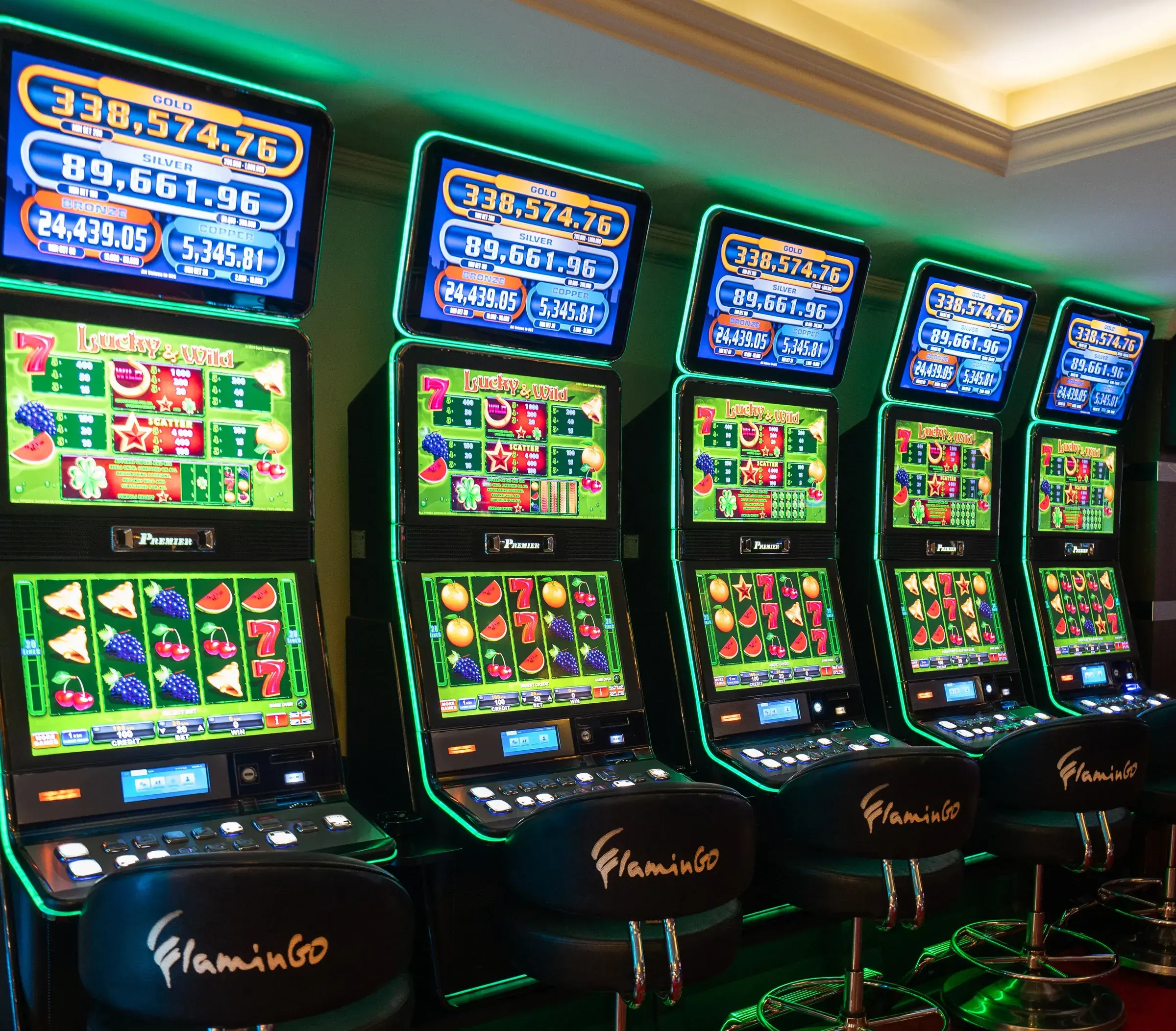 Five Lucky and Wild slot machines edged in green neon, each carrying the four tier jackpot board above the reels