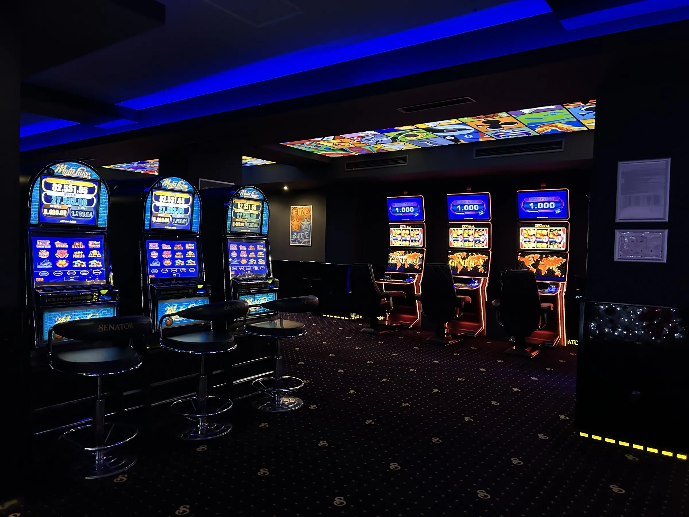 Two banks of slot machines facing each other across the carpet under blue cove lighting