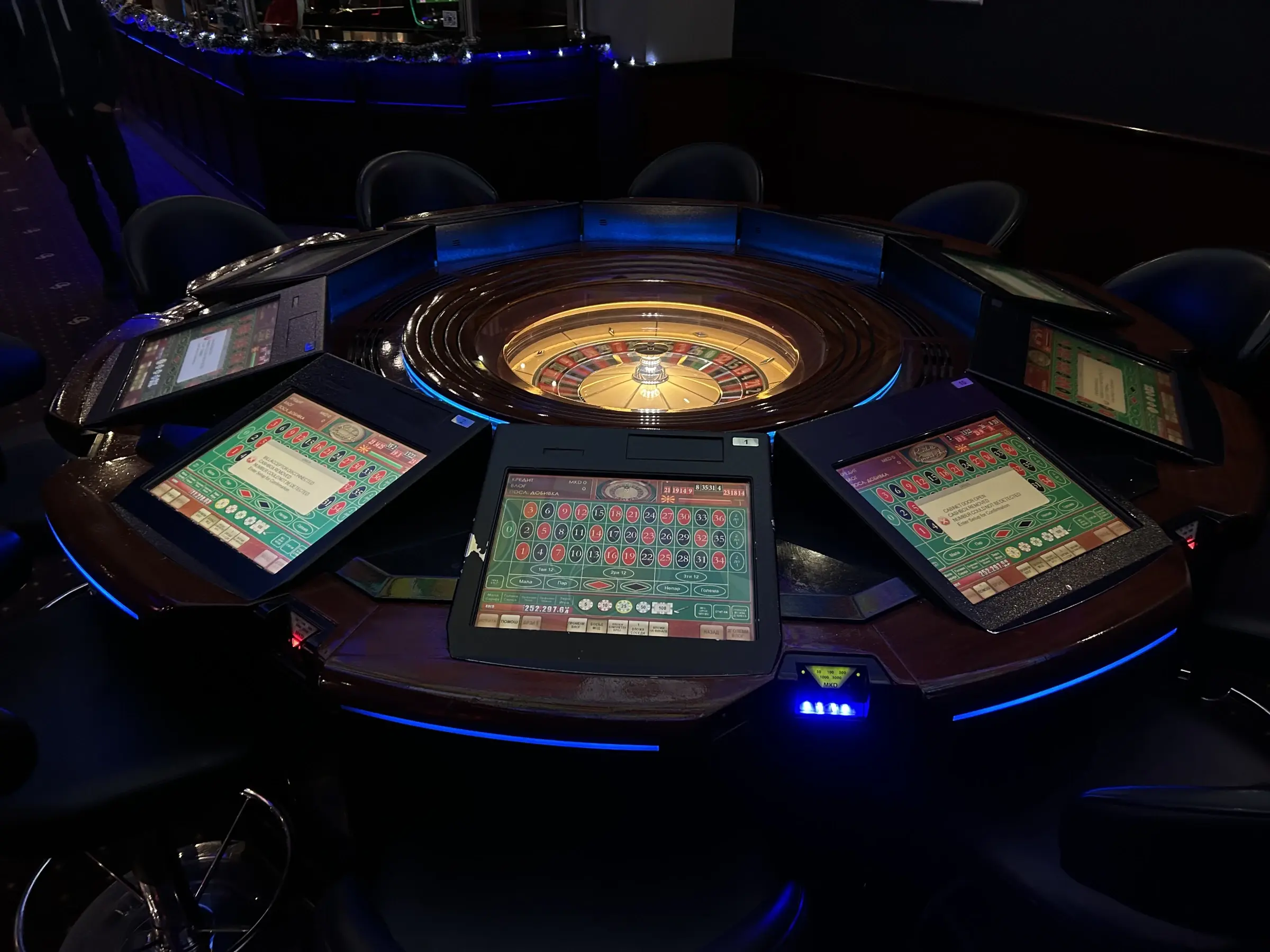 An electronic roulette table seen from above, the wheel at the centre and the player stations set around it