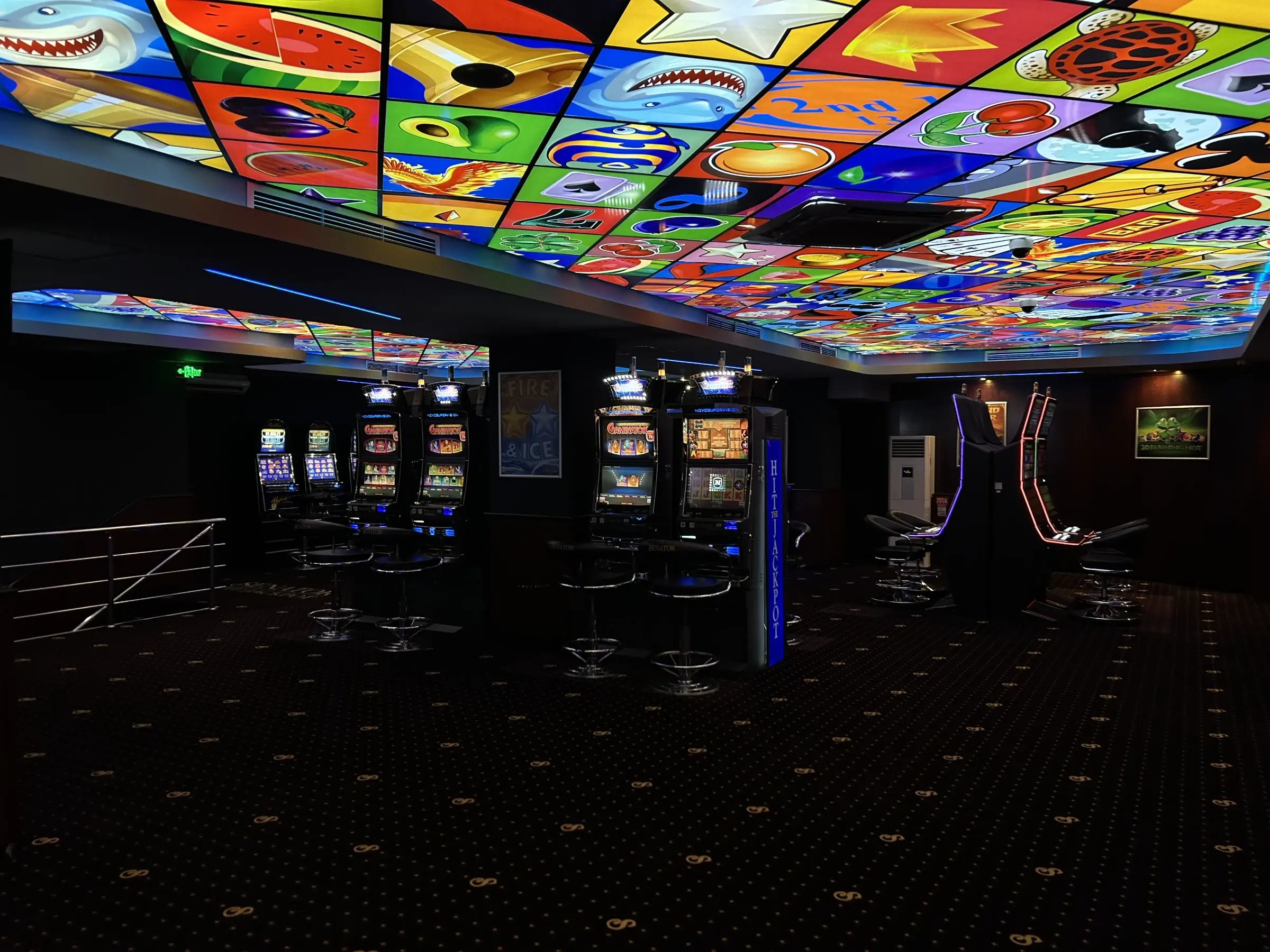 A Senator club floor under a backlit ceiling of fruit, card and sport symbols, slot machines along both walls