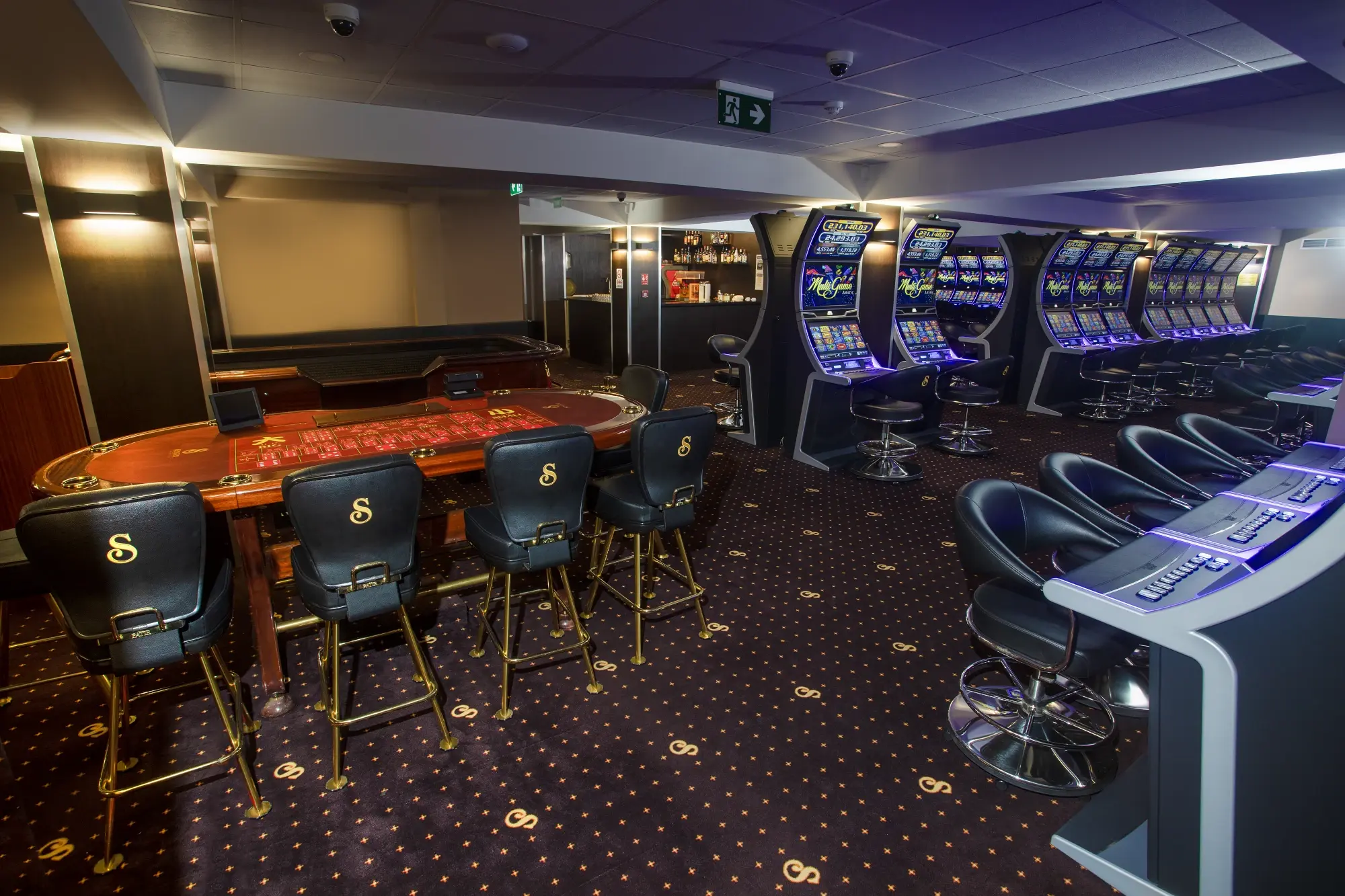 A red card table ringed by stools carrying the gold Senator monogram, a bar behind and a bank of slot machines to the right, Senator Club, Mauritius