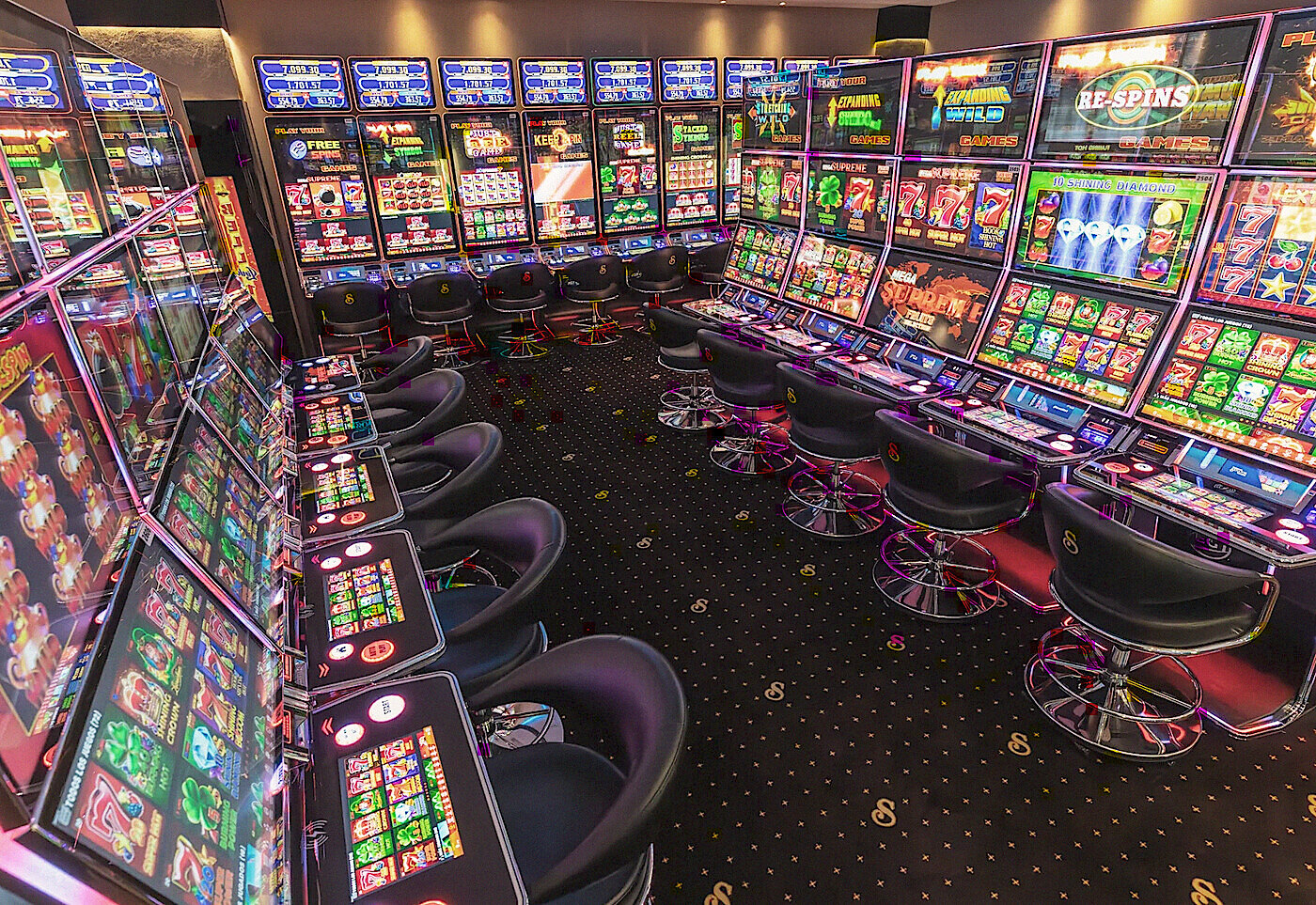 Two walls of slot machines meeting at the corner of a Senator gaming room, stools along both, Guatemala